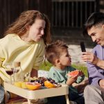 Smiling family having a picnic with fresh fruit on a sunny day, capturing memories.